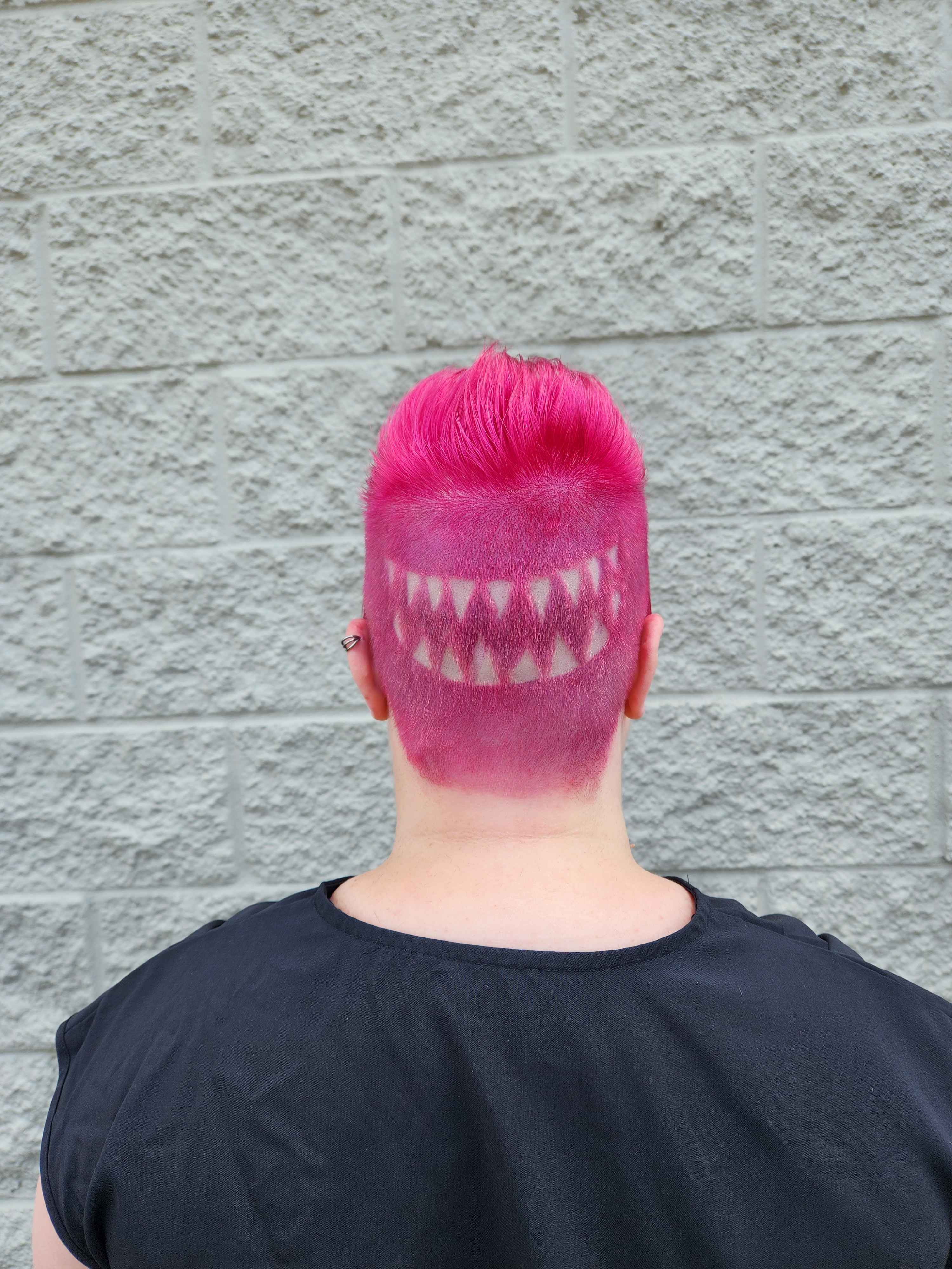 the back of the same client's head. in the center of the buzzcut portion is a silhouette of the first row of sharks teeth as a design that is shaved and dyed into the hair.