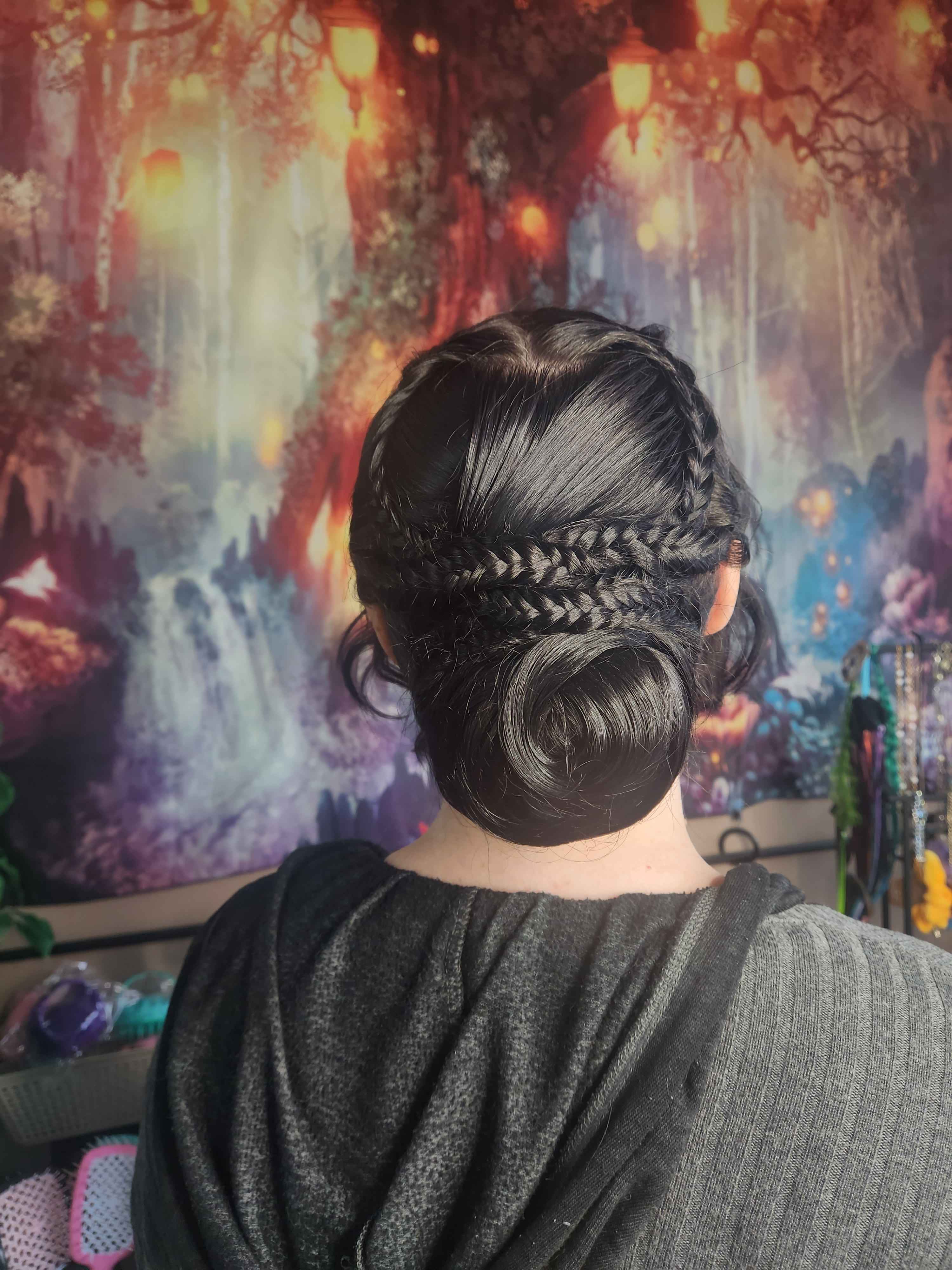 a client with black hair that is done in an up-do that consists of a low bun with accent braids